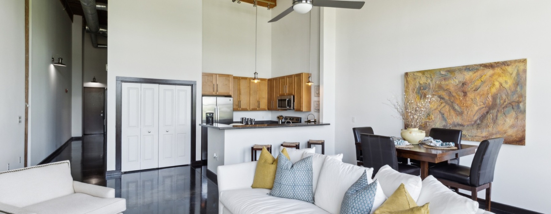 Contemporary open-layout interior showcasing a white sofa, minimalist dining setup, and a modern kitchen with wood cabinetry and tall ceilings, creating a warm, welcoming atmosphere; keywords: 2 bedroom apartments Greenville SC, apartments for rent Greenv